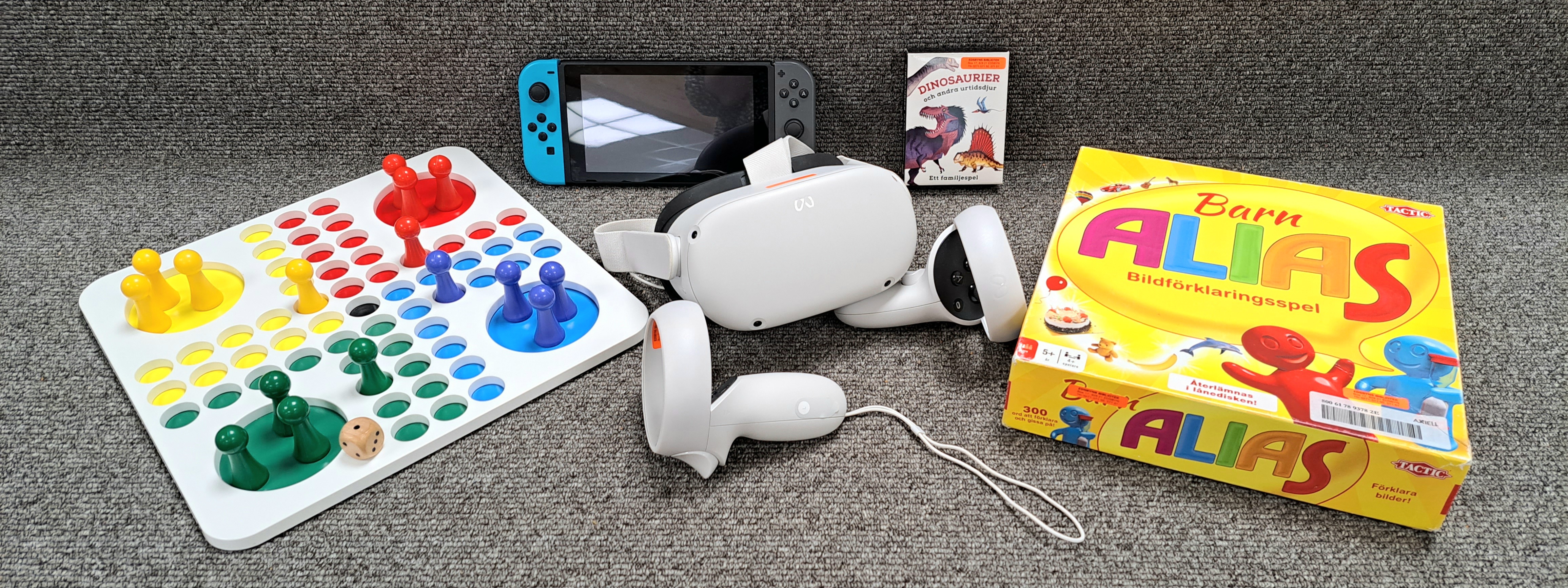 Ett fiaspel, en TV-spelkonsol, VR-glasögon med två handkontroller, ett dinosauriespel och ett barn-Alias-spel mot en grå bakgrund.