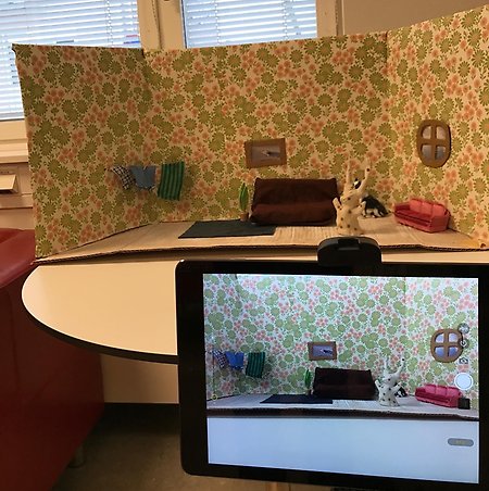 En iPad som fotograferar en "scen" med en lerfigur i ett vardagsrum.