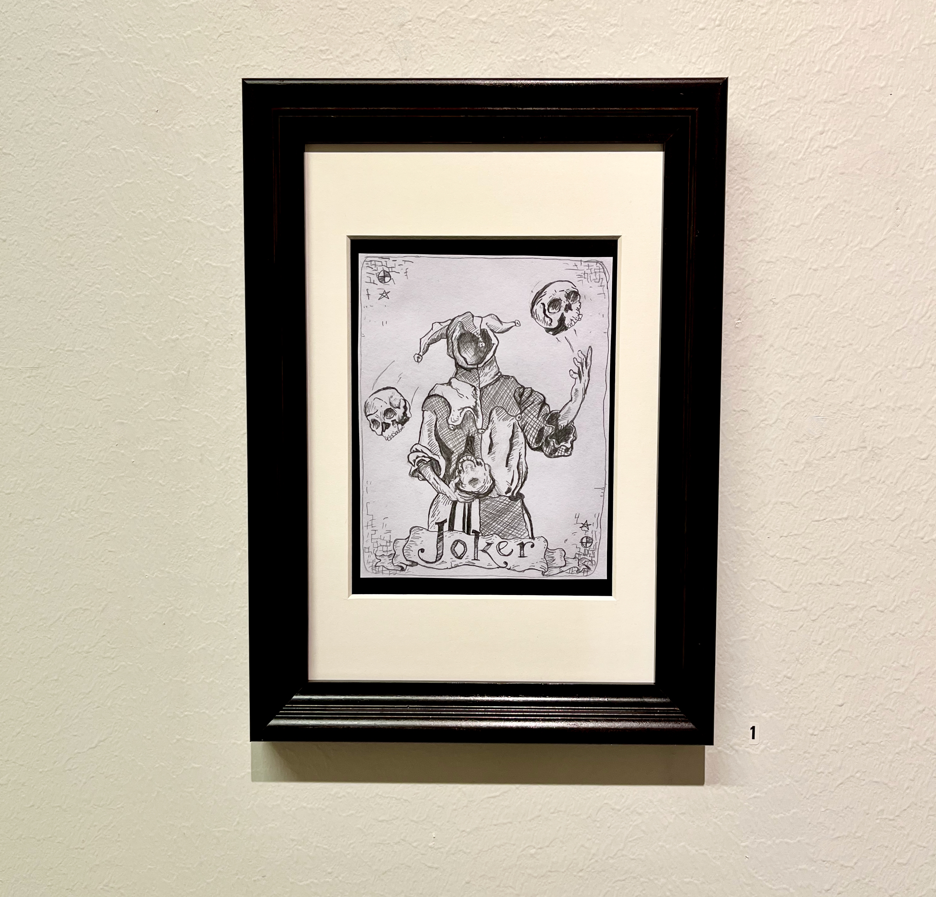 En figur utan ansikte i jokerkostym som jonglerar med tre dödsskallar. figuren är tecknad i gråtoner med blyerts och kol på en vit pappersbakgrund.