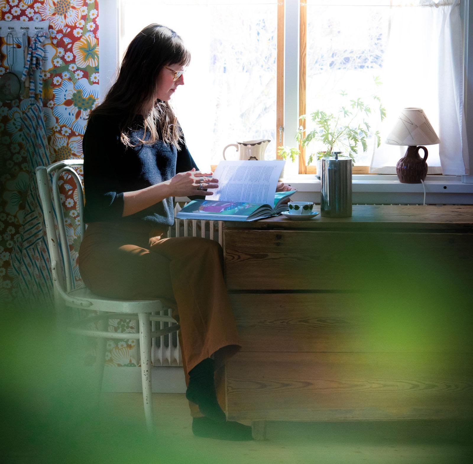 Elisabeth Embretsen sitter vid en byrå vid ett fönster och läser.
