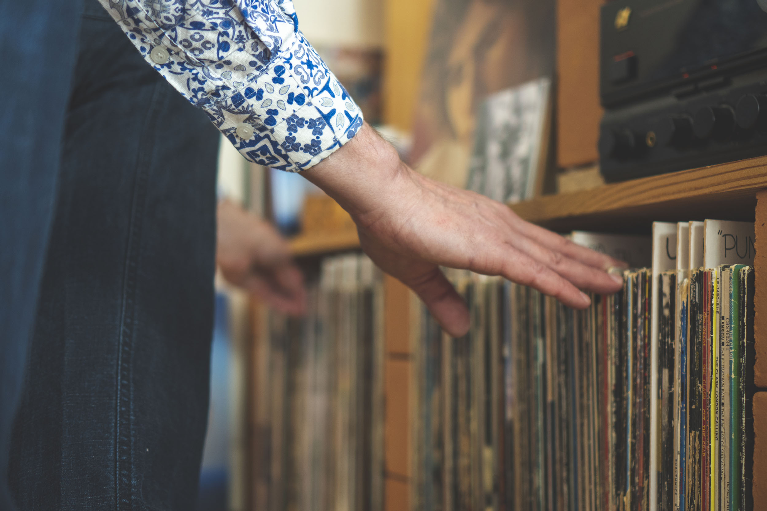 En hand bläddrar bland vinylskivor i en stereomöbel.