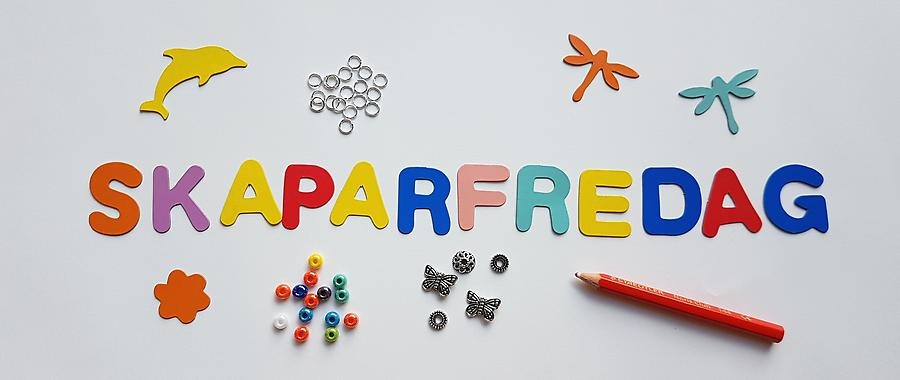 Ordet SKAPARFREDAG skrivet med bokstäver av papp, omgivet av pärlor, utstansade pappfigurer och en penna.