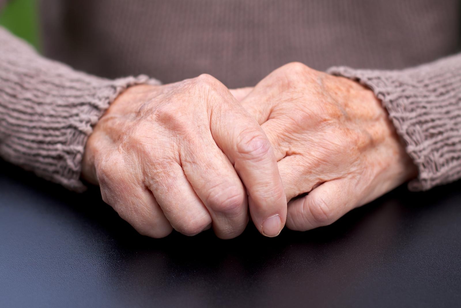 En äldre människa håller i sin egen hand i knät.