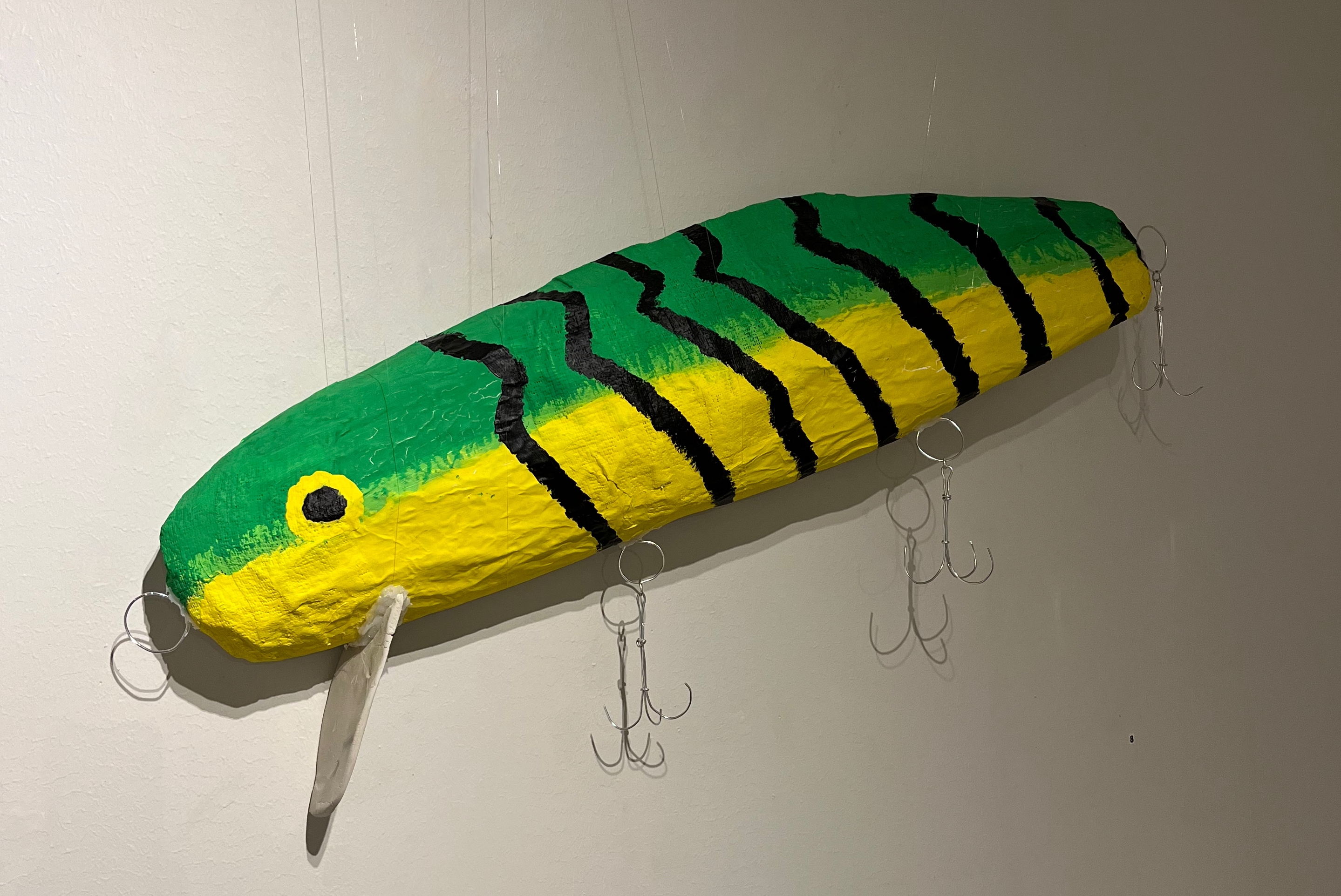En mycket stor version av en wobbler som används vid fiskning av gädd, gös och lax. Wobblern har en grön rygg och gul buk med svarta ränder runt kroppen. Tre stora krokar hänger från wobblerns buk.