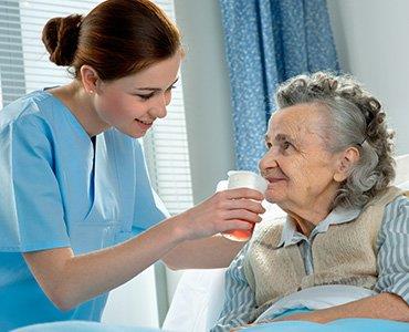 Undersköterska hjälper äldre kvinna att dricka ur glas.