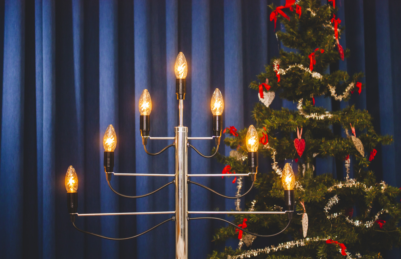 Tänd ljusstake och julgran framför en mörkblå bakgrund.