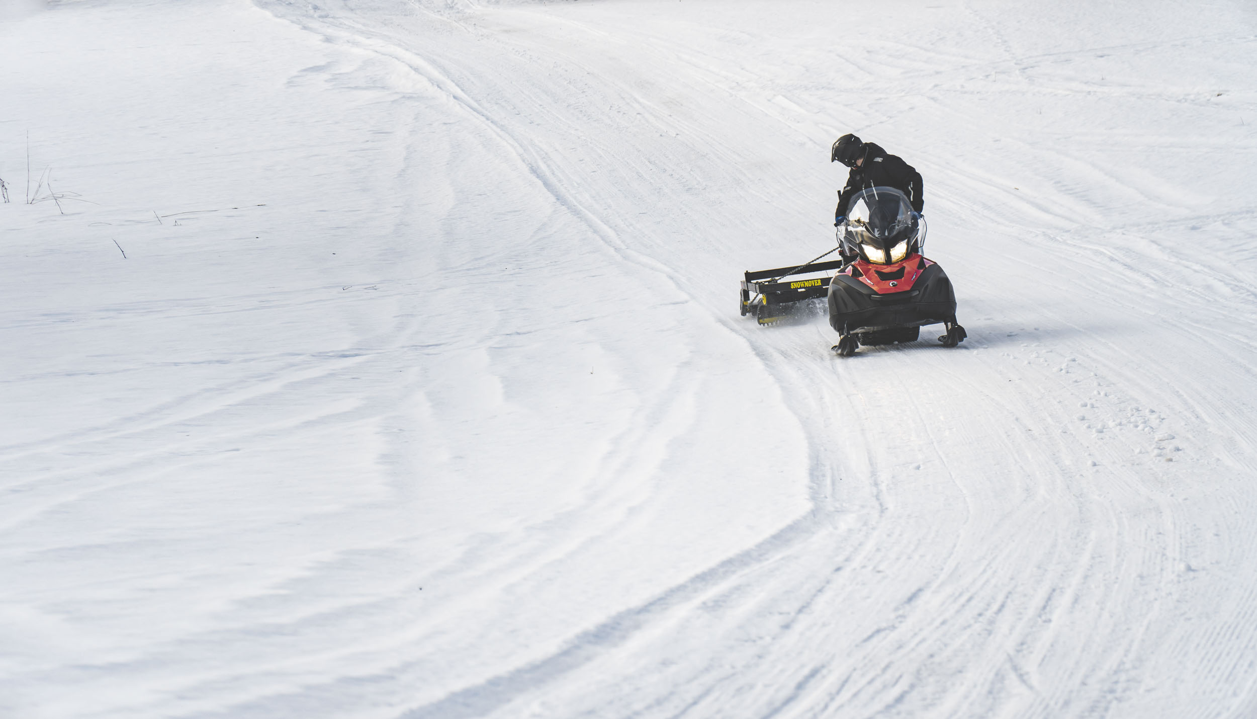 Joakim kör skoter över ett öppet snötäckt fält, dragandes på en snöskotersladd.