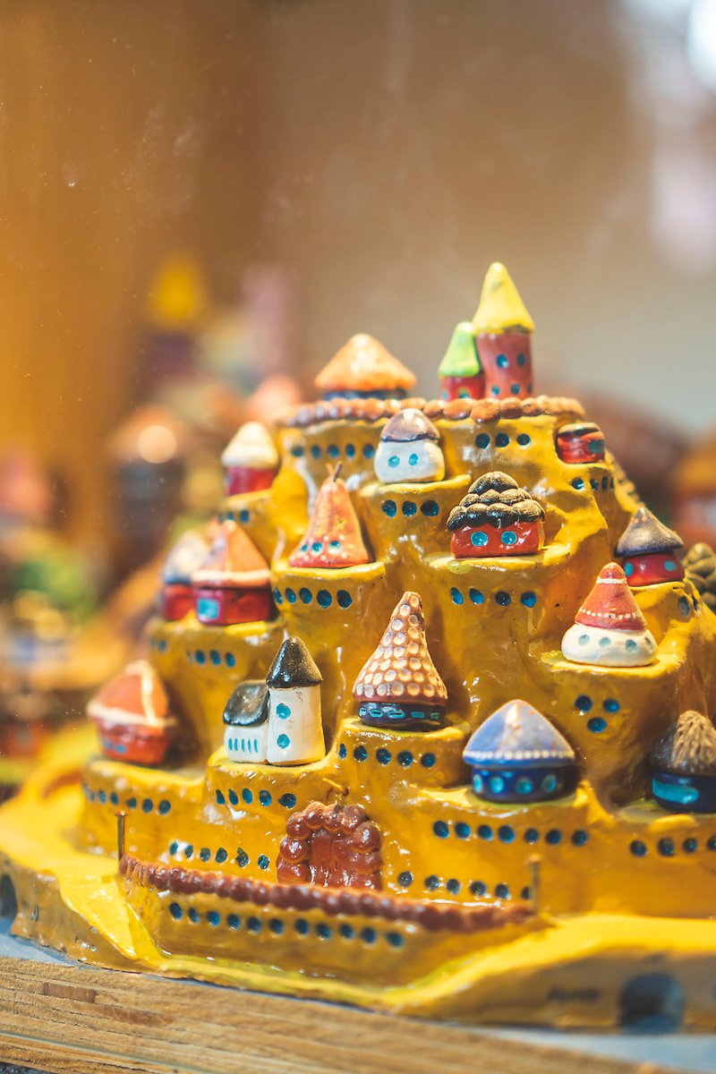 Konstverk i lera som föreställer en gul kulle med små hus på.