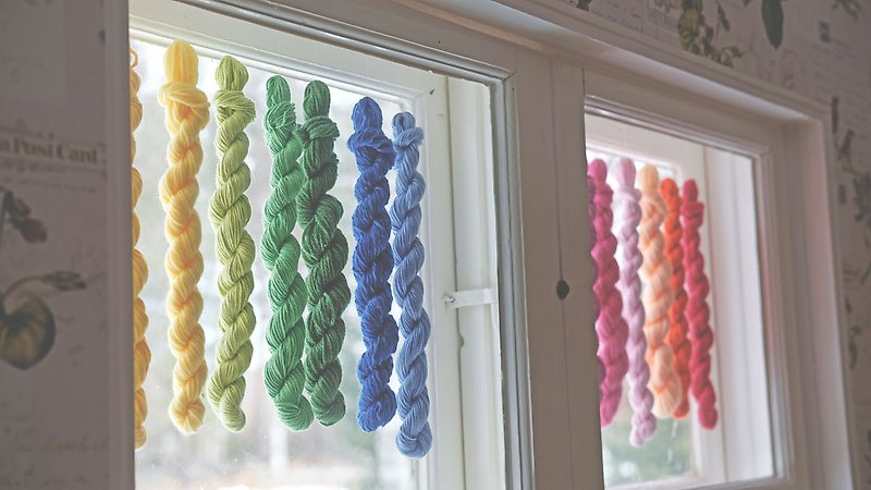 Garnspiraler i olika färger som hänger i ett fönster.
