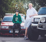 Albin och Ture står lutade mot sina EPA-traktorer på en asfaltsparkering, med grönska i bakgrunden.