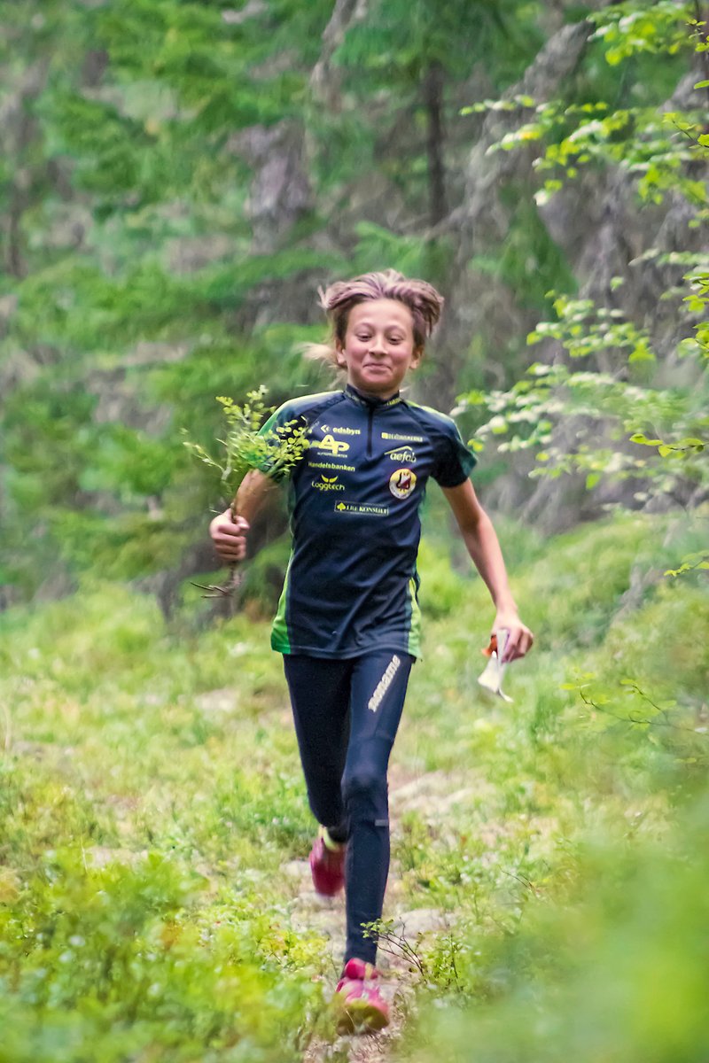 En ung kille springer i skogen iförd Alfta ÖSA-OK-kläder och håller en växt i handen.