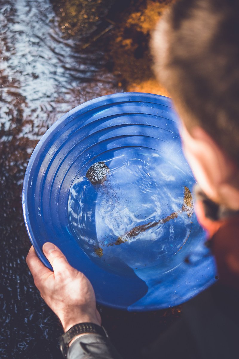 Joakim Larsson håller en blå plastskål med vatten och lite grus i botten.