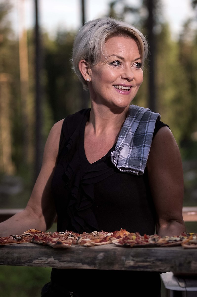 Lena Hisved håller en nygräddad pizza på en träplanka.
