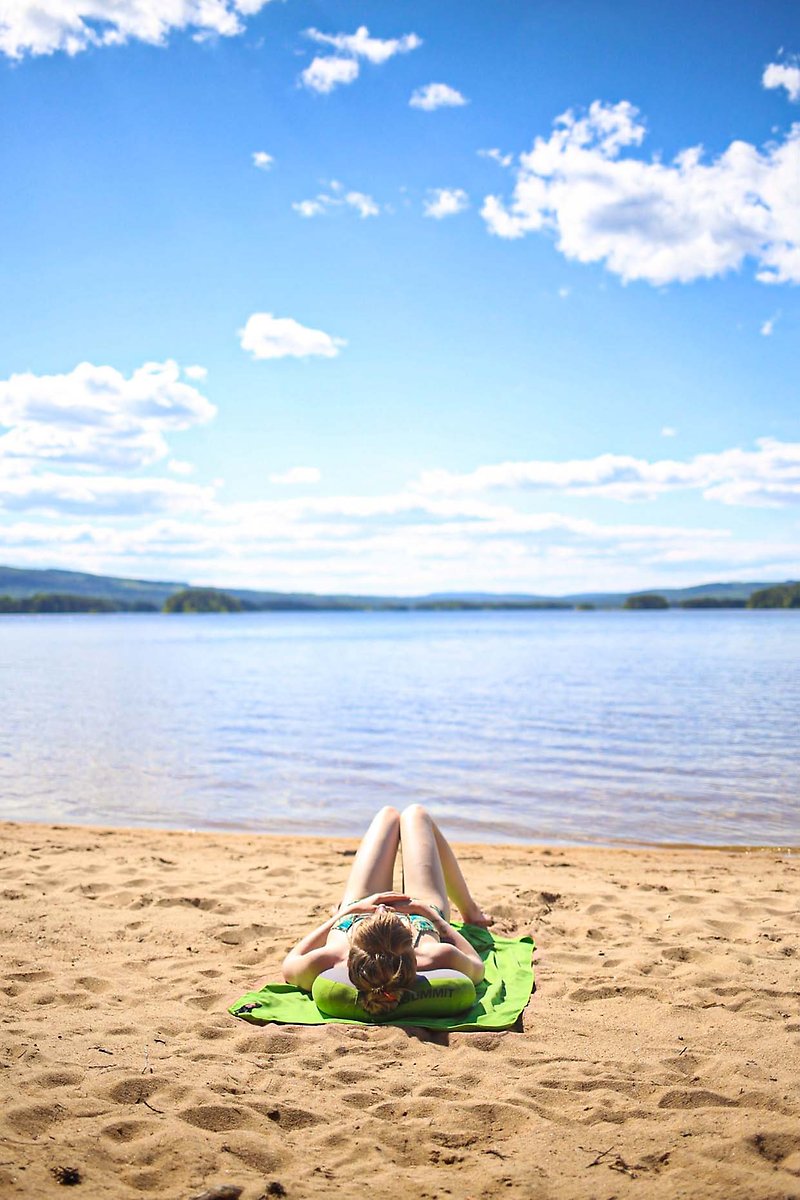 En tjej solar på en badstrand vid vattenbrynet under blå himmel.
