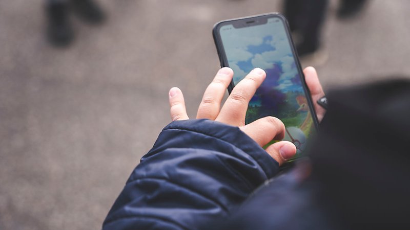 Ett barns händer knappar på en mobiltelefon med spelet Pokemon Go på skärmen.
