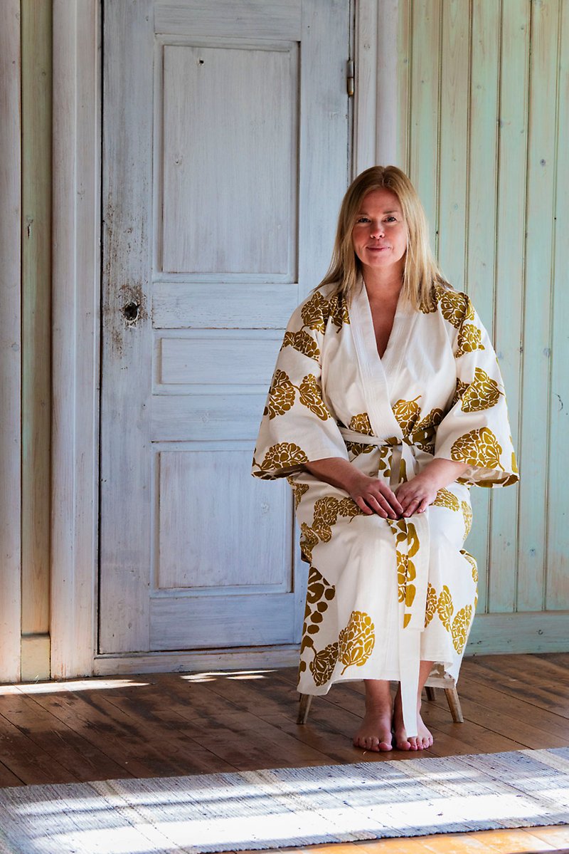 Malin Svedberg sitter på en stol i ett gammalt hus iförd en vit kimono med guldfärgade mönster på.