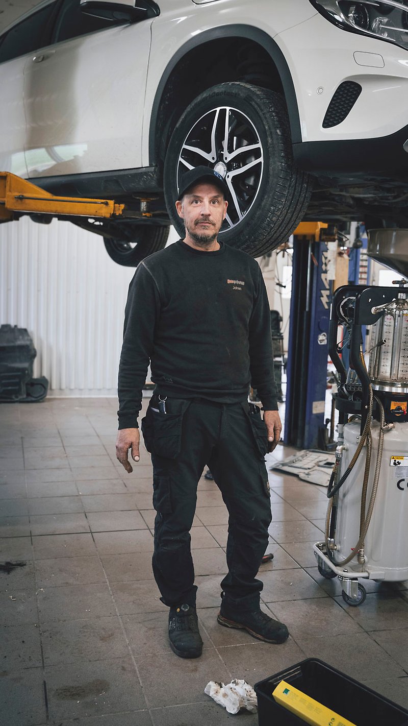 Johan Öst står i arbetsbyxor framför en upphöjd bil i sin verkstad.