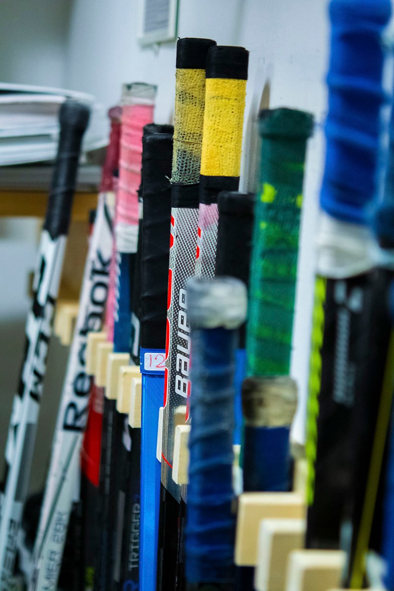 Hockeyklubbor i olika färger uppställda mot en vägg.