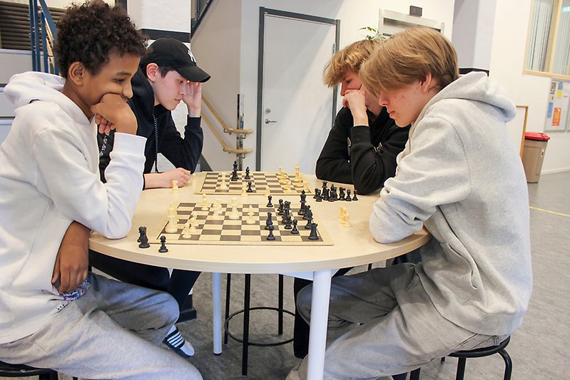 Fyra tonåringar spelar schack runt ett bord.