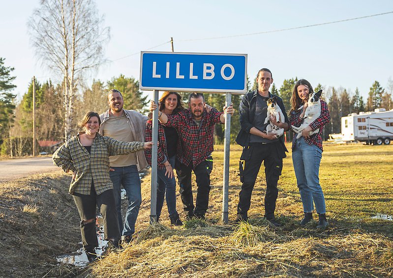 Familjen Bengtsberg står runtomkring en blå vägskylt som det står "Lillbo" på.