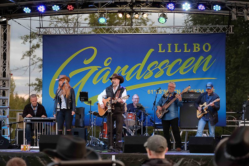 Ron Redmond med band spelar på scenen. På ett stort skynke bakom bandet står det "Lillbo Gårdsscen".