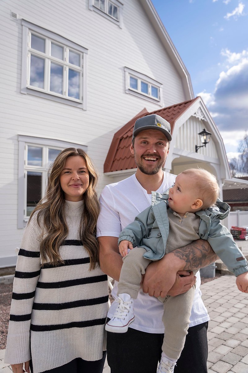 Johanna Jonsson och Markus Fagerhof står framför sitt nyrenoverade hus. Markus håller deras barn i famnen.