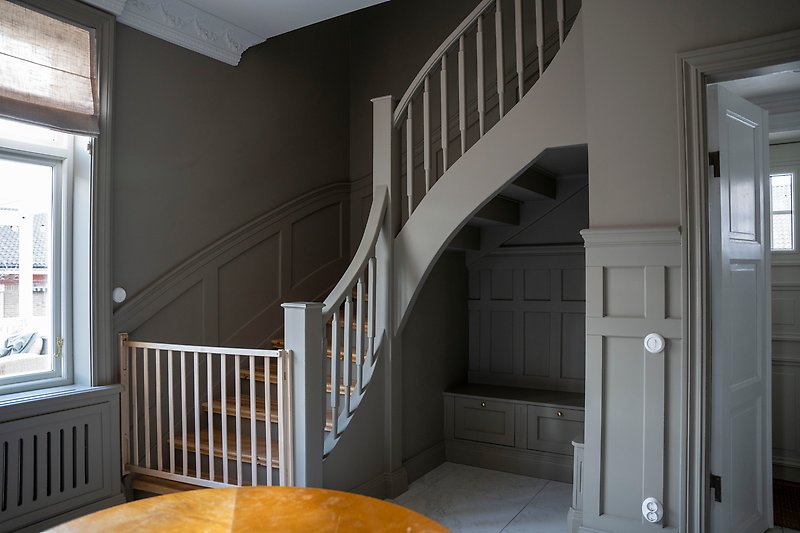 En hall med grå väggar och grå paneler, och en trappa upp till övervåningen.