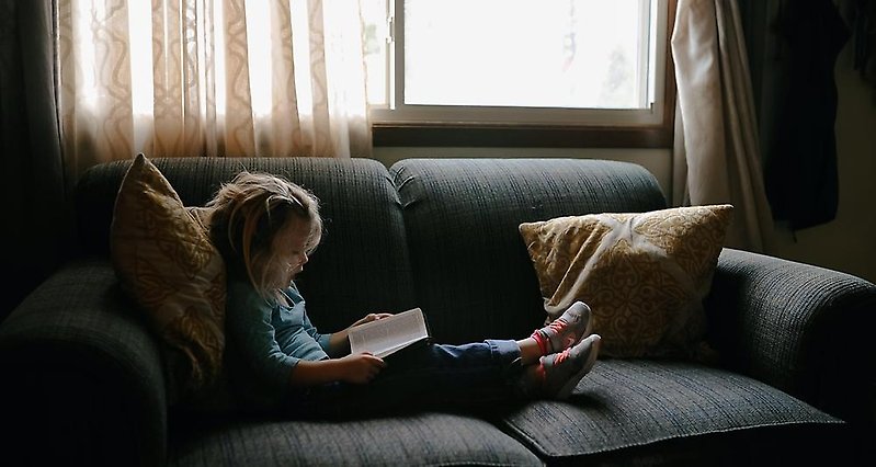 ett barn som sitter på en soffa med en bok