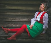 Susanne poserar i sin röd-grön-vita julutstyrsel framför en timmervägg.