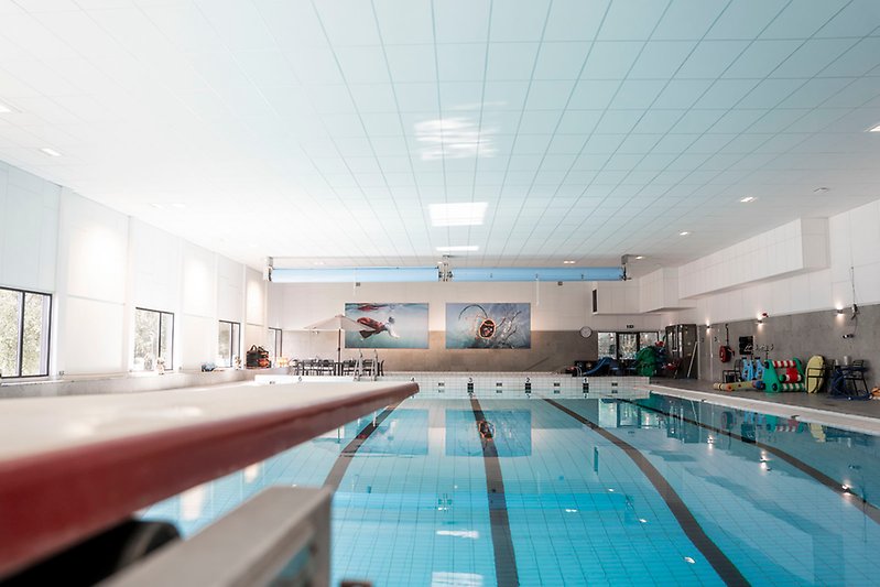 Vy över hela stora bassängen i simhallen, med en trampolin i förgrunden som sticker ut över vattnet.