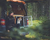 Christian sitter längst bak i sin van ute i skogen tillsammans med sin hund och båda blickar ut över skogsvägen.