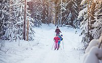 En barnfamilj åker längdskidor i en snötäckt skog.