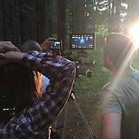 Ungdomar står runt en filmkamera ute i skogen