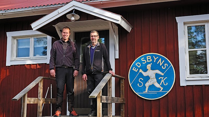 Jens Eliasson och Sture Hansson står framför en röd stuga med Edsbyns SK:s skylt på väggen.