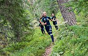 Tre unga människor springer genom skogen iförd Alfta ÖSA-OK-kläder.