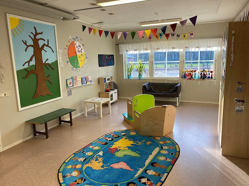 Stora rummet på förskolan, bilden visar en leksaksbåt, kök med bord, en stor oval matta, en liten soffa och en garderob
