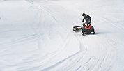 Joakim kör skoter över ett öppet snötäckt fält, dragandes på en snöskotersladd.