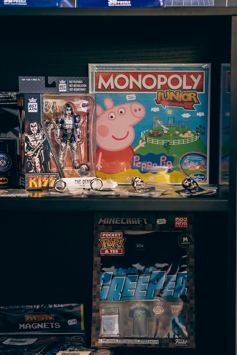 I en svart hylla står Kiss-figurer, en Minecraft-T-shirt, Pac-man-magneter och ett Greta Gris-monopolspel.